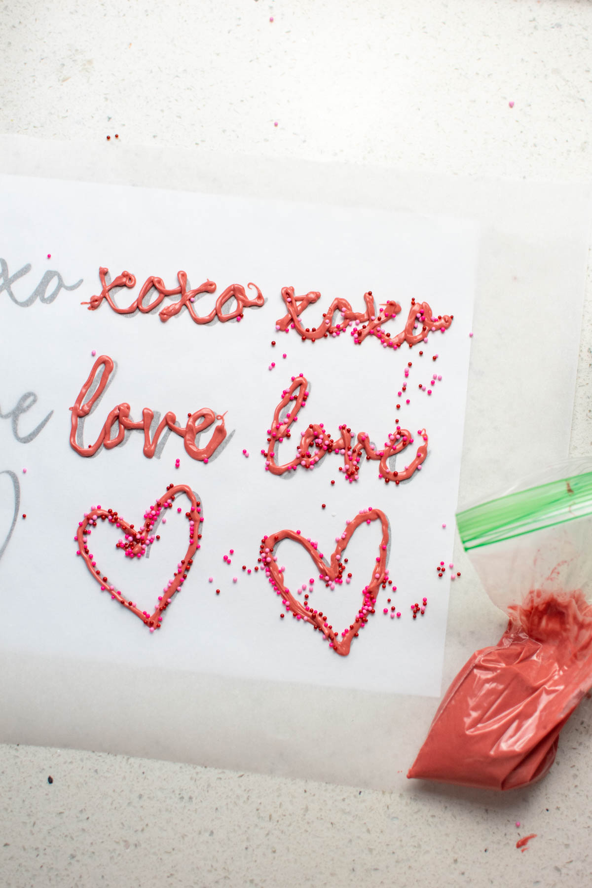 Melted candy wafer cupcake toppers spelling love, xoxo, and a heart on parchment paper.