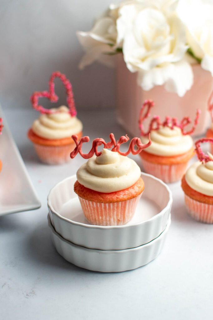 Strawberry Valentine's Day cupcakes in ramekin dishes and on table with pink flower vase in background.