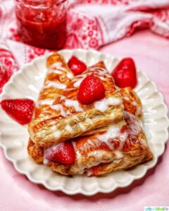 Stack of strawberry turnovers white glaze and fresh berries on a white plate.