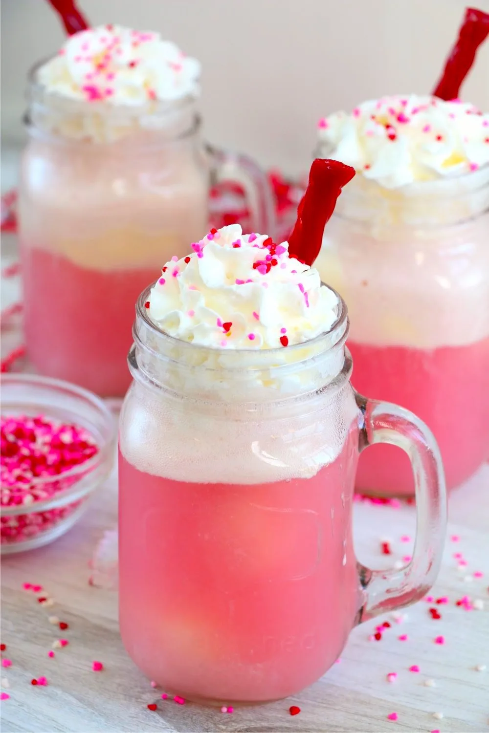 3 Cherry floats in mason jars with whipped cream and pink sprinkles.