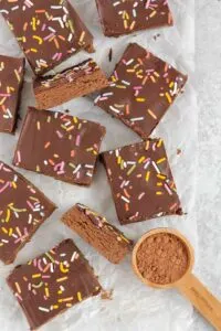 Several chocolate protein bars with colorful sprinkles on white parchment paper.