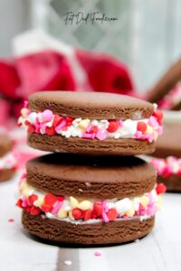 A stack of chocolate sandwich cookies with pink, red, and white sprinkles.