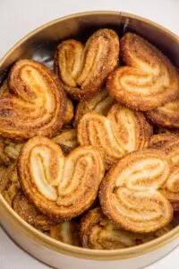 Several heart-shaped cinnamon palmiers piled in a bread basket.