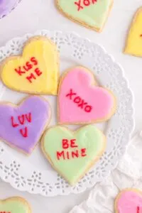 Yellow, pink, purple, and green conversation heart cookies on a white plate.