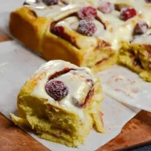 Several cranberry cinnamon rolls with white glaze on white parchment paper.