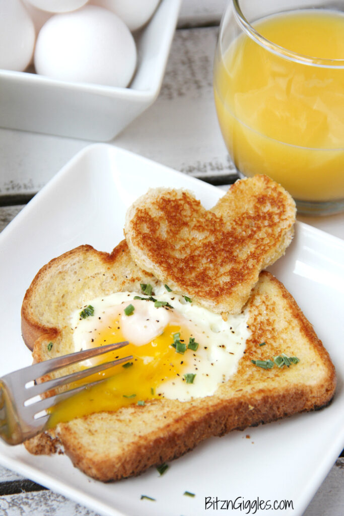 Toast with heart-shaped cut out with egg cooked inside on white plate.