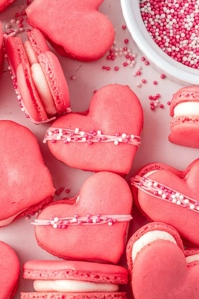 Heart-shaped pink macarons with sprinkle decorations on pink background.