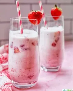 Two glasses of Korean strawberry milk with red and white straws and strawberry garnish.