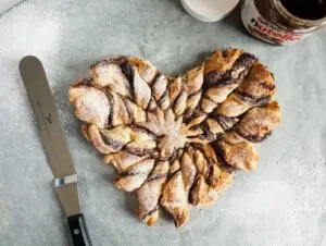 Heart made of Nutella puff pastry twists on gray countertop with spatula nearby.