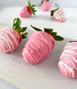 Several pink chocolate covered strawberries on a white serving platter.