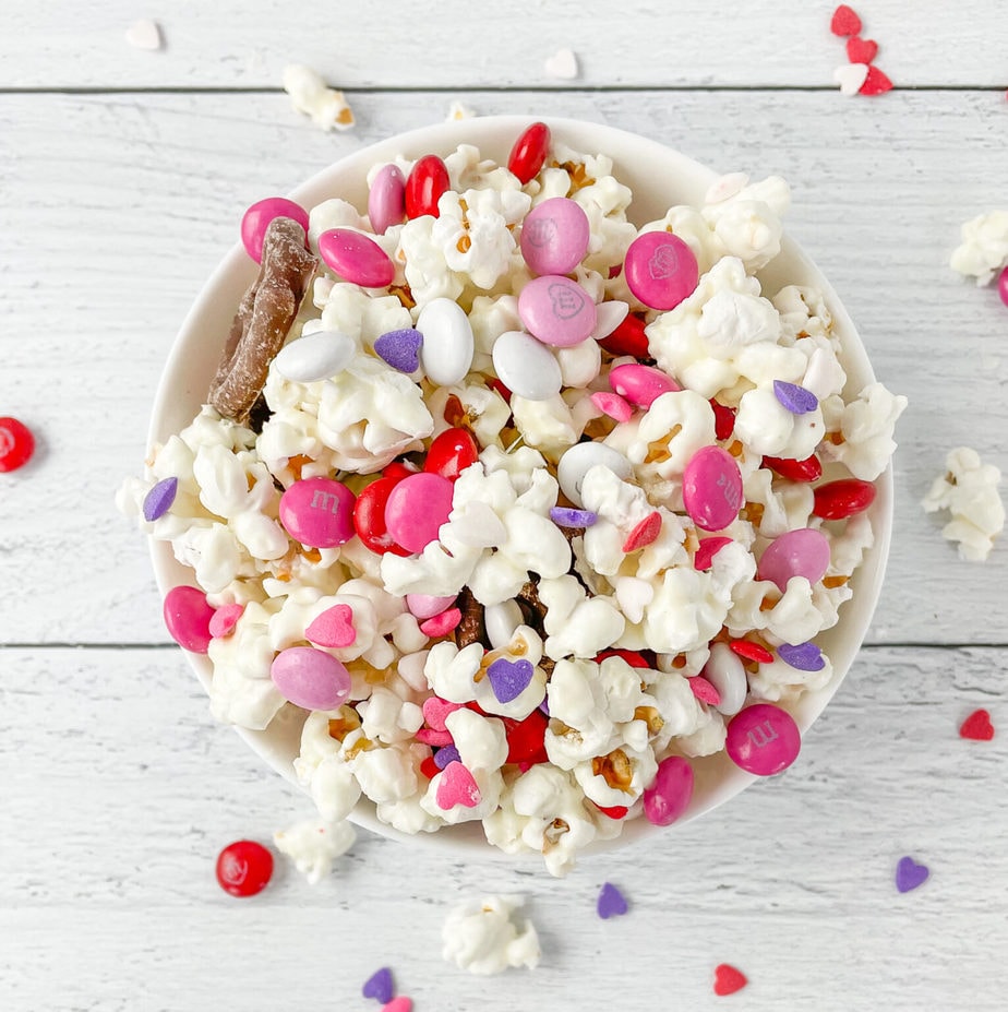 Popcorn snack mix with pink, white, and purple candies in a white bowl.