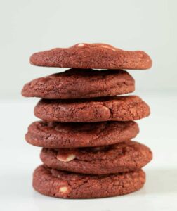 A tall stack of red velvet chocolate chip cookies on a white background.