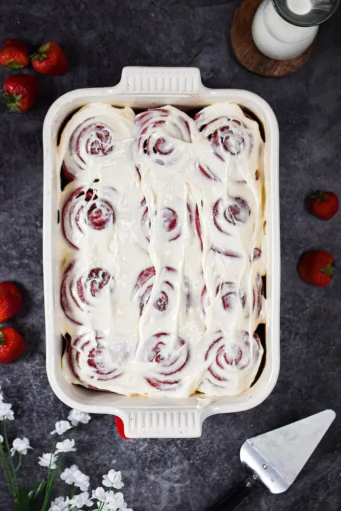 A large white casserole baking dish filled with red velvet cinnamon rolls with white glaze.