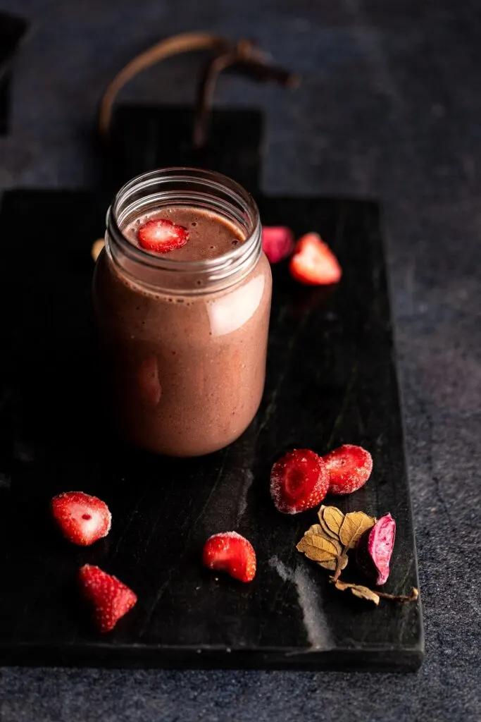 Strawberry banana chocolate smoothie in a glass mason jar next to fresh strawberries.