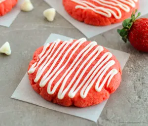 Strawberry cake mix cookies with white glaze on squares of parchment paper.