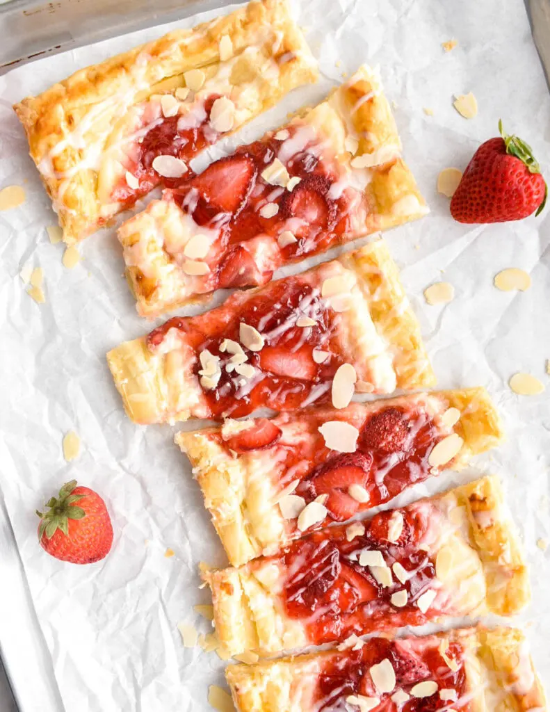 Strawberry cream cheese danish cut into slices on white parchment paper with fresh strawberries.