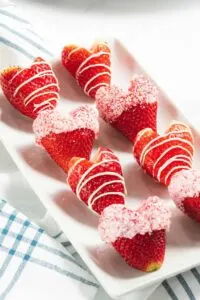 Several strawberries cut into the shape of a heart with chocolate drizzle and sprinkles.