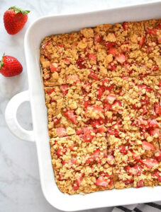 Strawberry oat breakfast bars in a large white casserole baking dish with fresh strawberries.