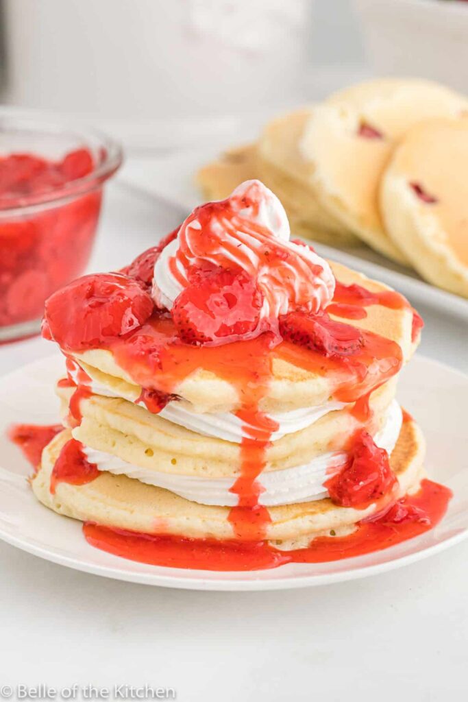 Stack of pancakes with strawberry syrup and fresh berries on a white plate.
