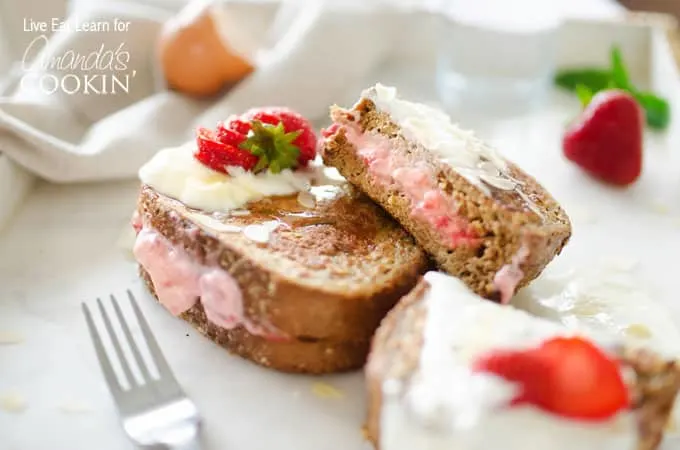 Two pieces of strawberry stuffed french toast on counter with fresh strawberries and fork nearby.