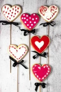 Heart-shaped sugar cookies on sticks with black bows and pink and red icing.
