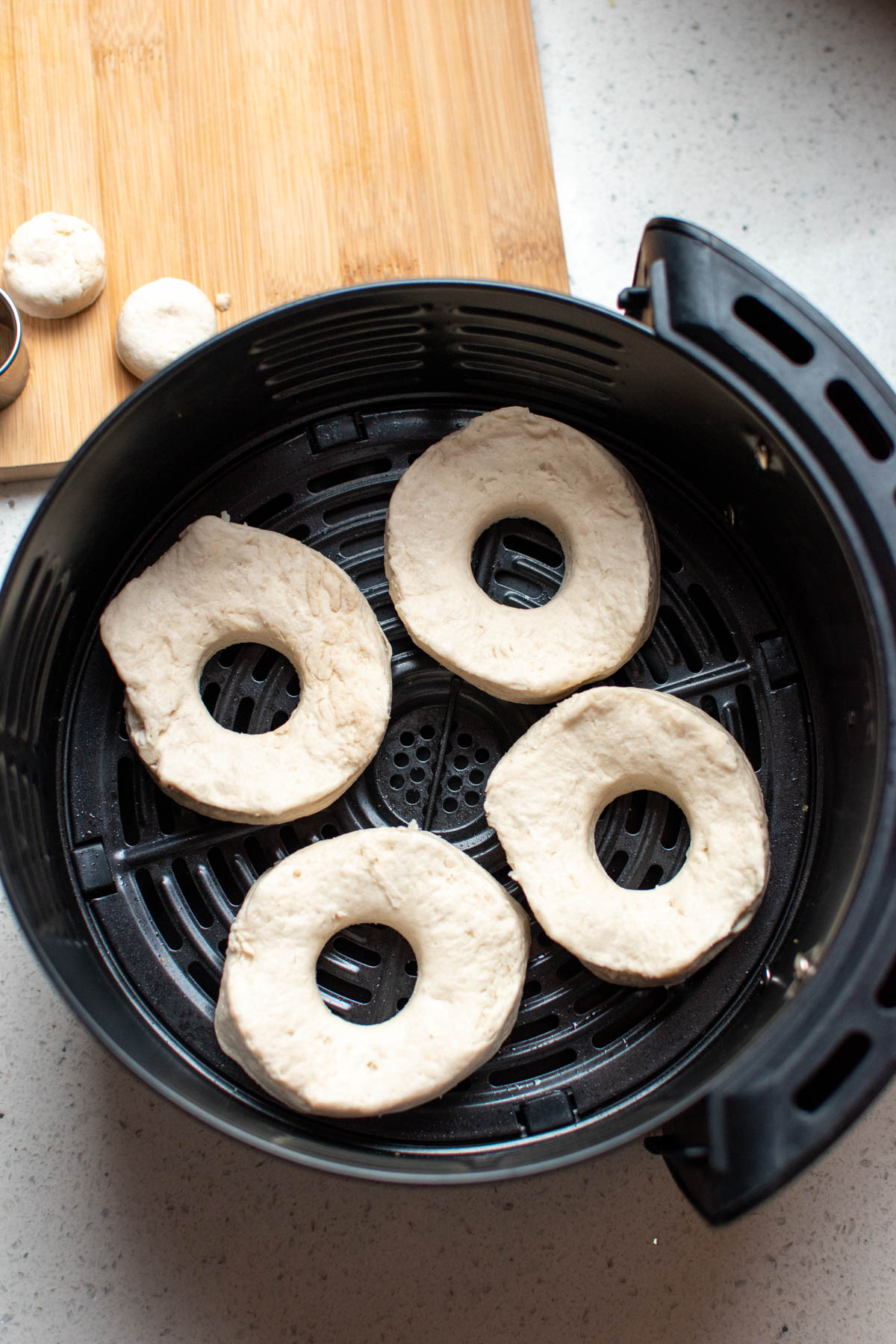 Four raw biscuit donuts in black air fryer basket on quartz counter.