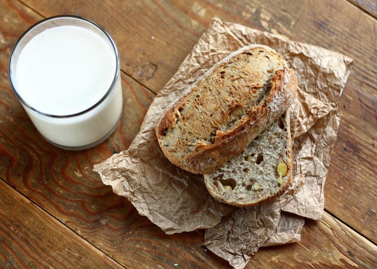 A crusty loaf of bread on parchment paper and a glass of milk.