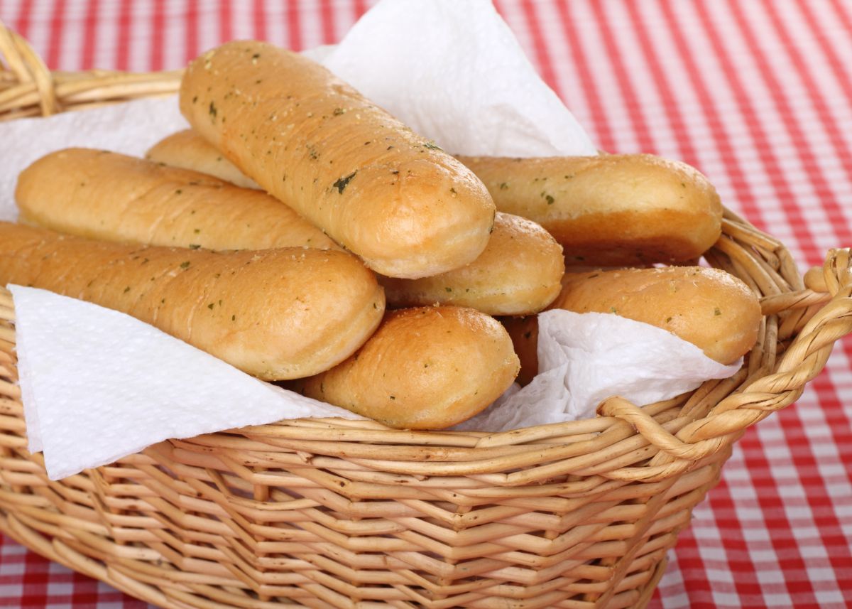 Several breadsticks in a large wicker basket on a red and white tablecloth.