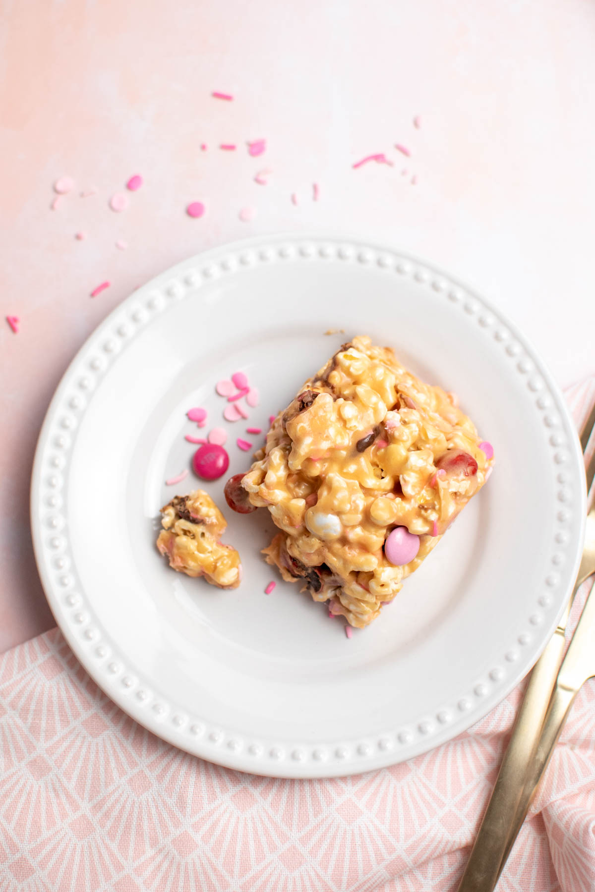 Piece of caramel popcorn cake on white plate with pink sprinkles and candies scattered around.
