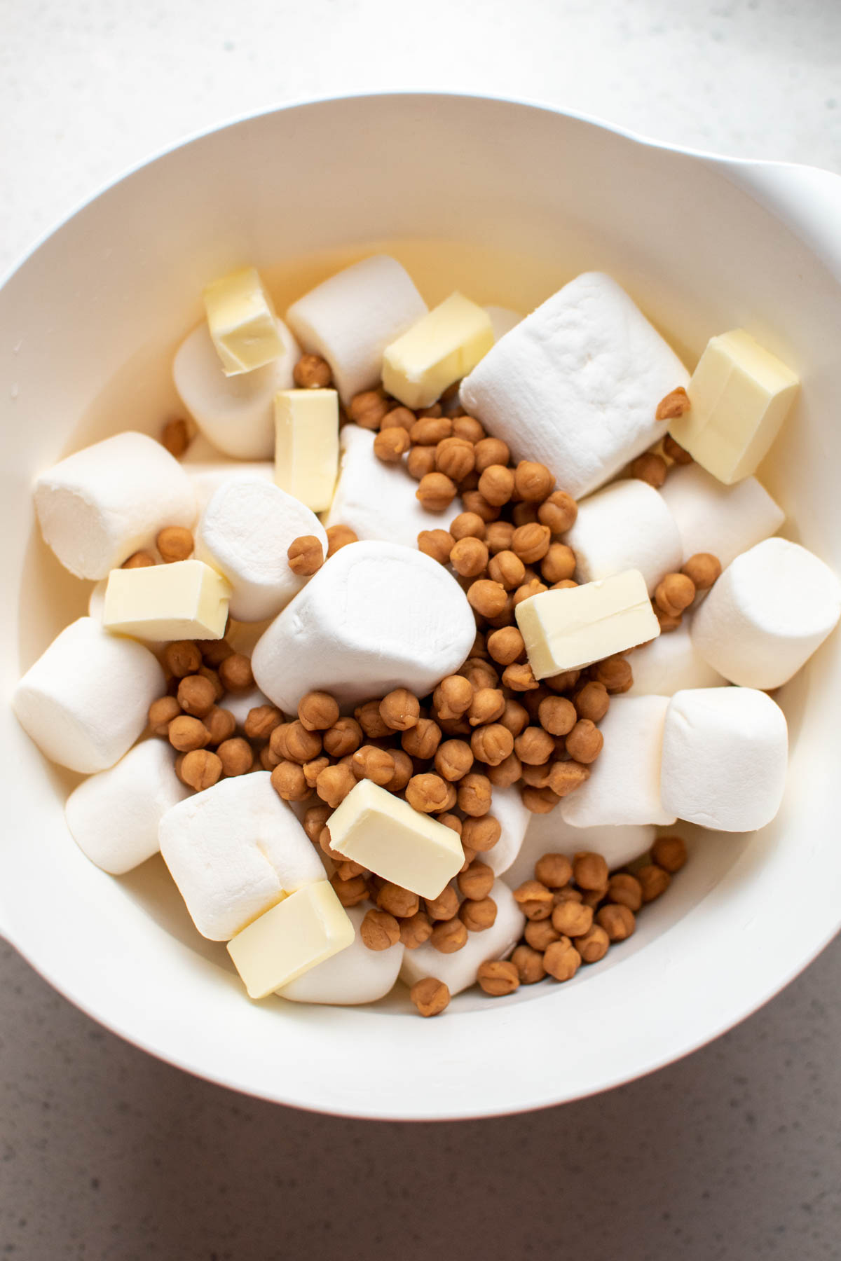 Marshmallows, caramel bits, and cubed butter in large white mixing bowl.