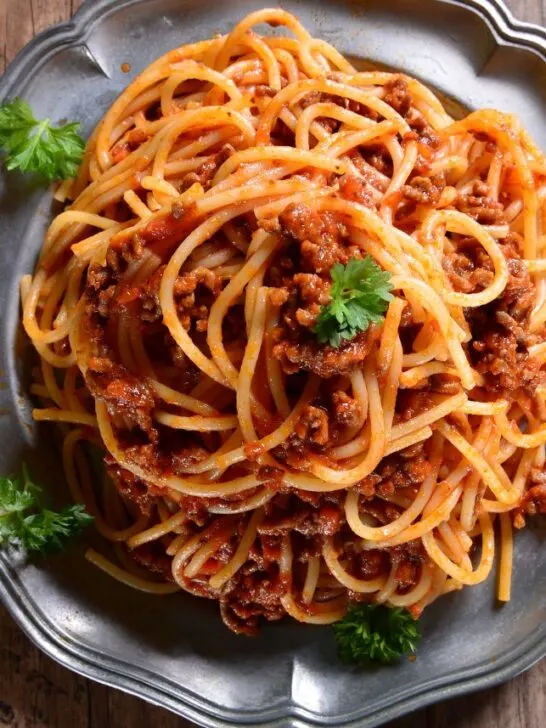 A large gray plate filled with spaghetti and meat sauce with green garnish.