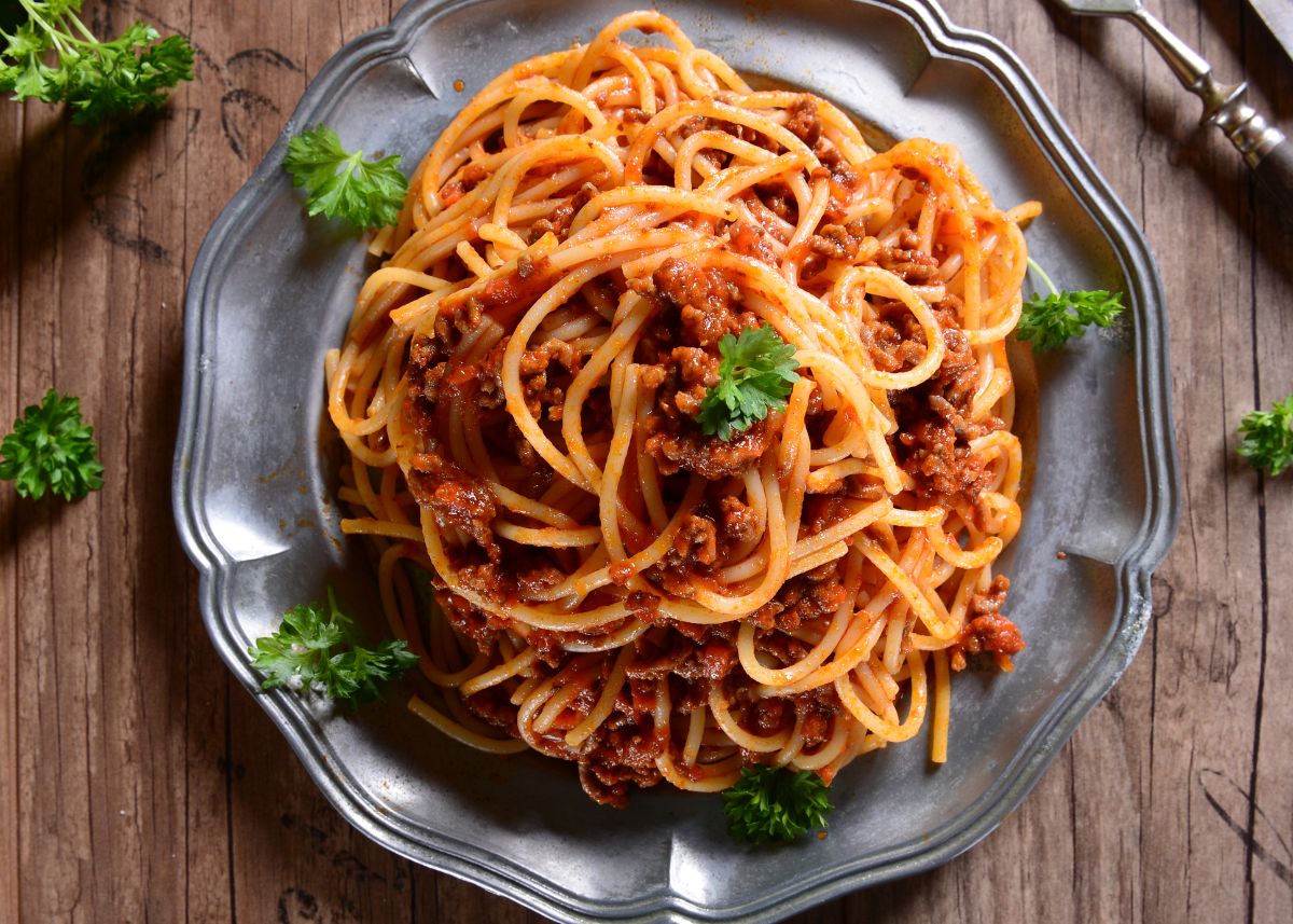 A large gray plate filled with spaghetti and meat sauce with green garnish.