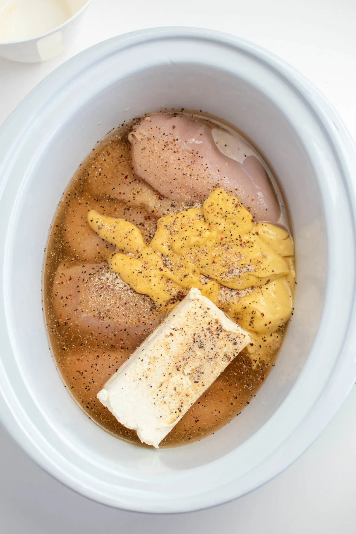 Block of cream cheese, cream of chicken soup, and raw chicken breasts in Crock Pot insert.
