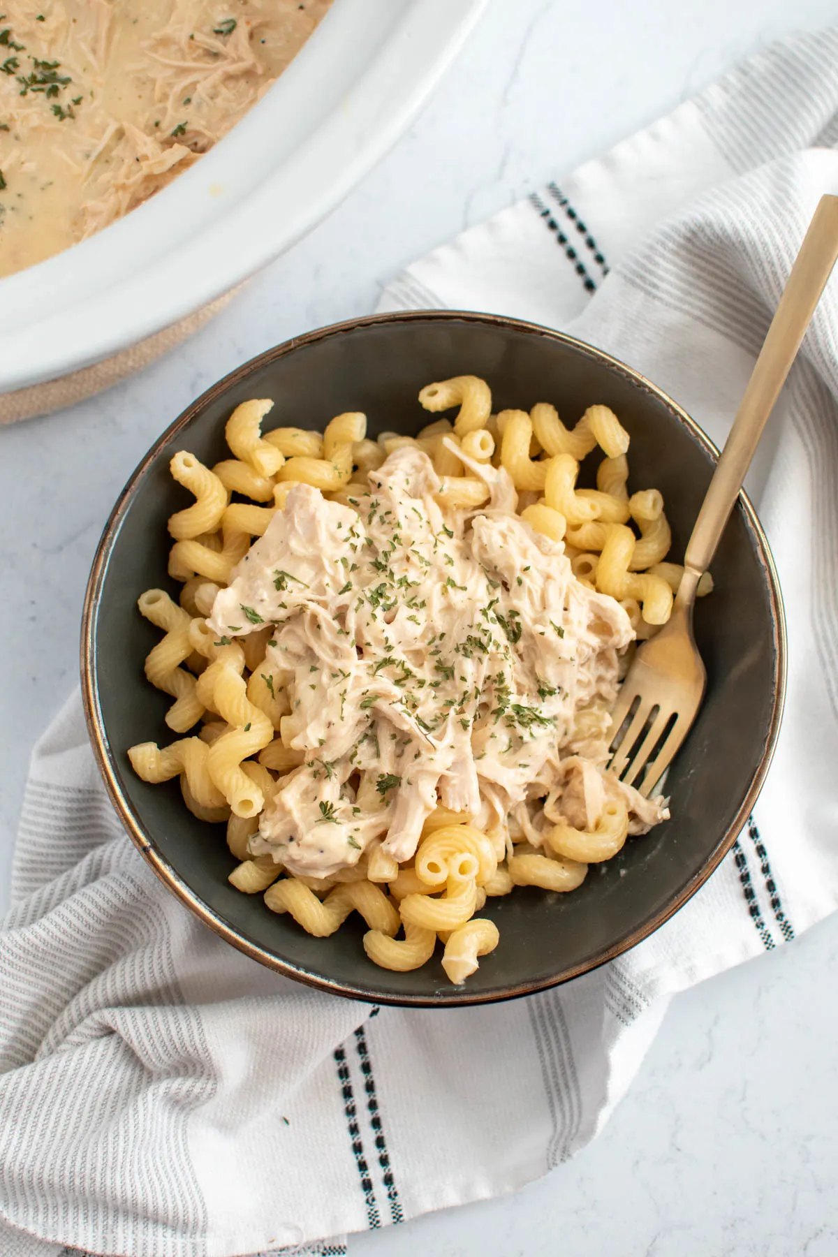 Bowl of pasta with creamy Italian chicken and fork on striped kitchen towel.