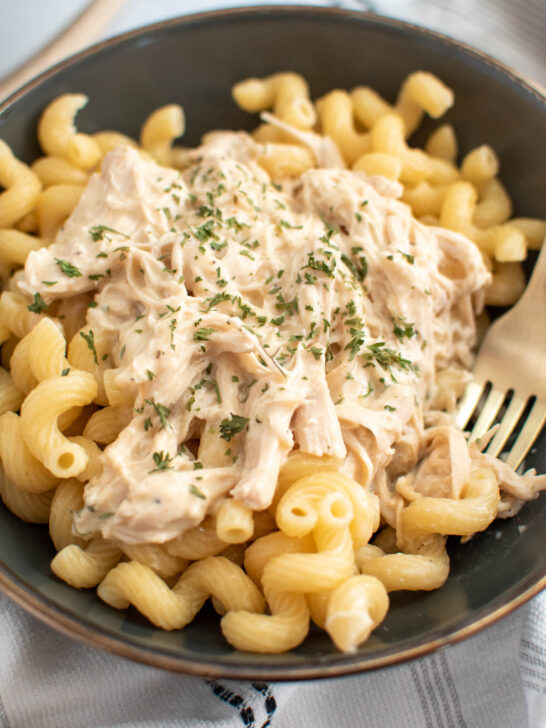 Fork rests in bowl of pasta with creamy Italian chicken on top.