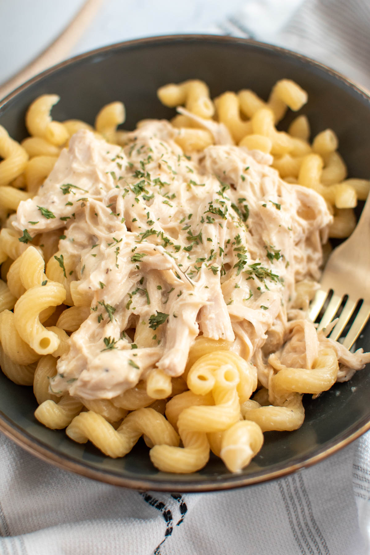 Fork rests in bowl of pasta with creamy Italian chicken on top.