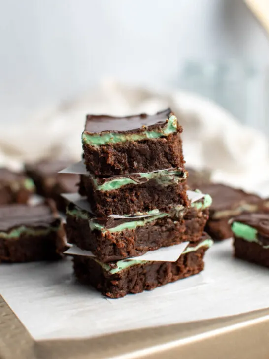 Mint brownies with chocolate ganache stacked on top of each other on parchment paper.