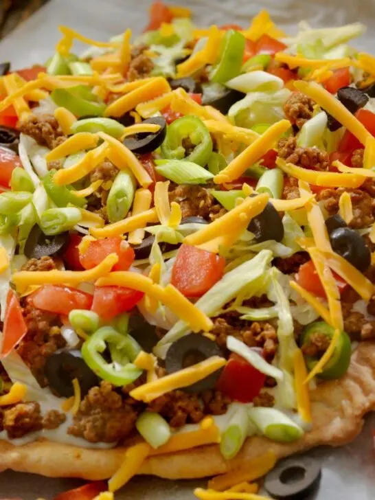 Flat bread taco salad with taco meat, cheese, tomatoes, olives, and lettuce.