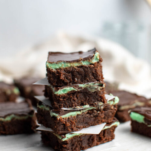 Mint brownies with chocolate ganache stacked on top of each other on parchment paper.