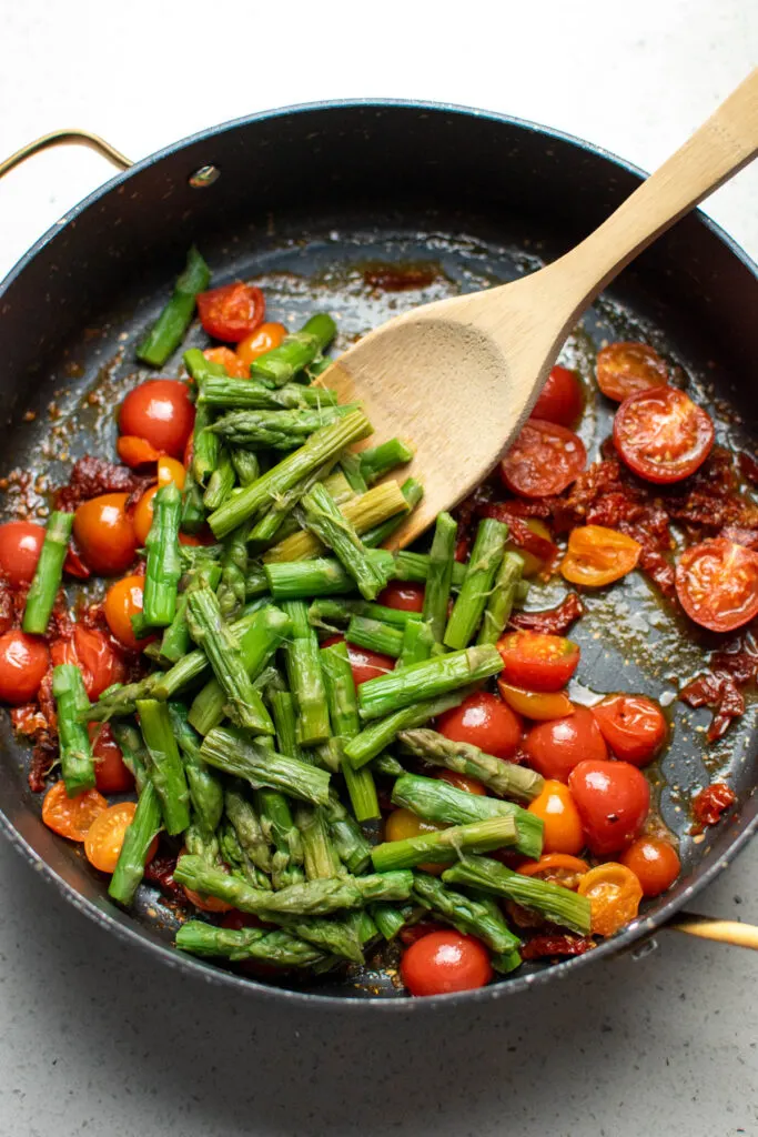 Chopped asparagus in large black skillet with fresh and sun-dried tomatoes.