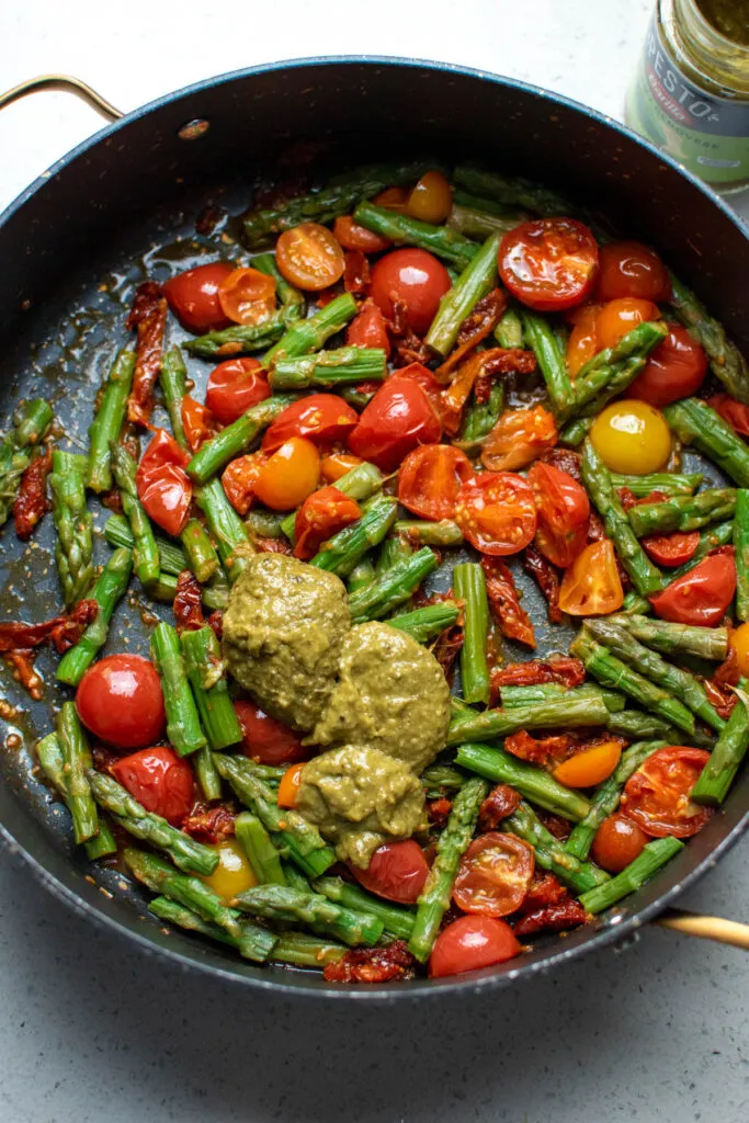 Several spoonfuls of basil pesto in large skillet with other vegetables.