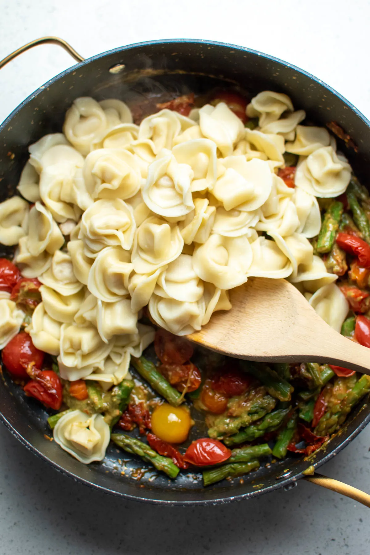 Cooked tortellini in large black skillet with tomatoes and asparagus.