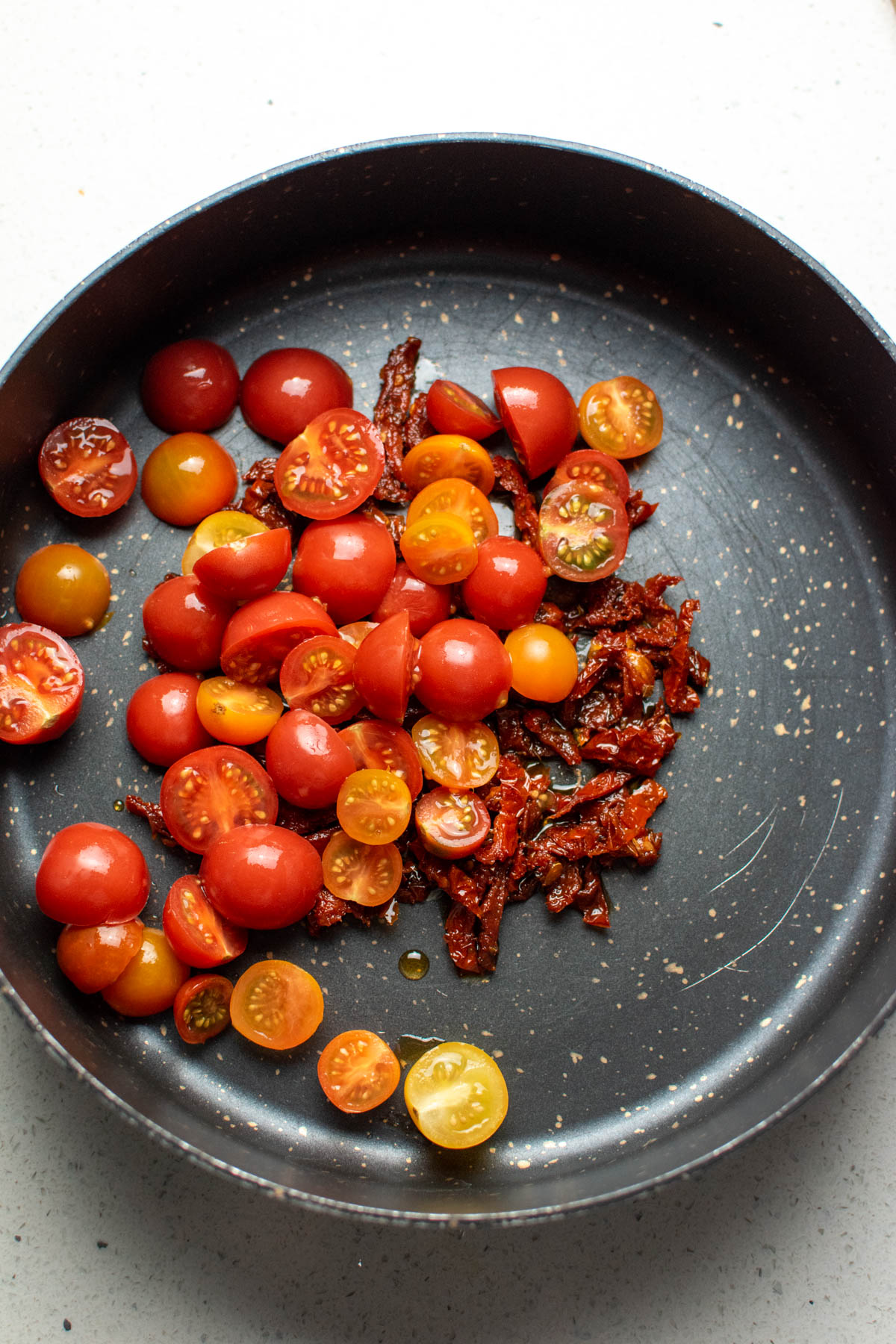 Cut cherry tomatoes and sun dried tomatoes in large black skillet.