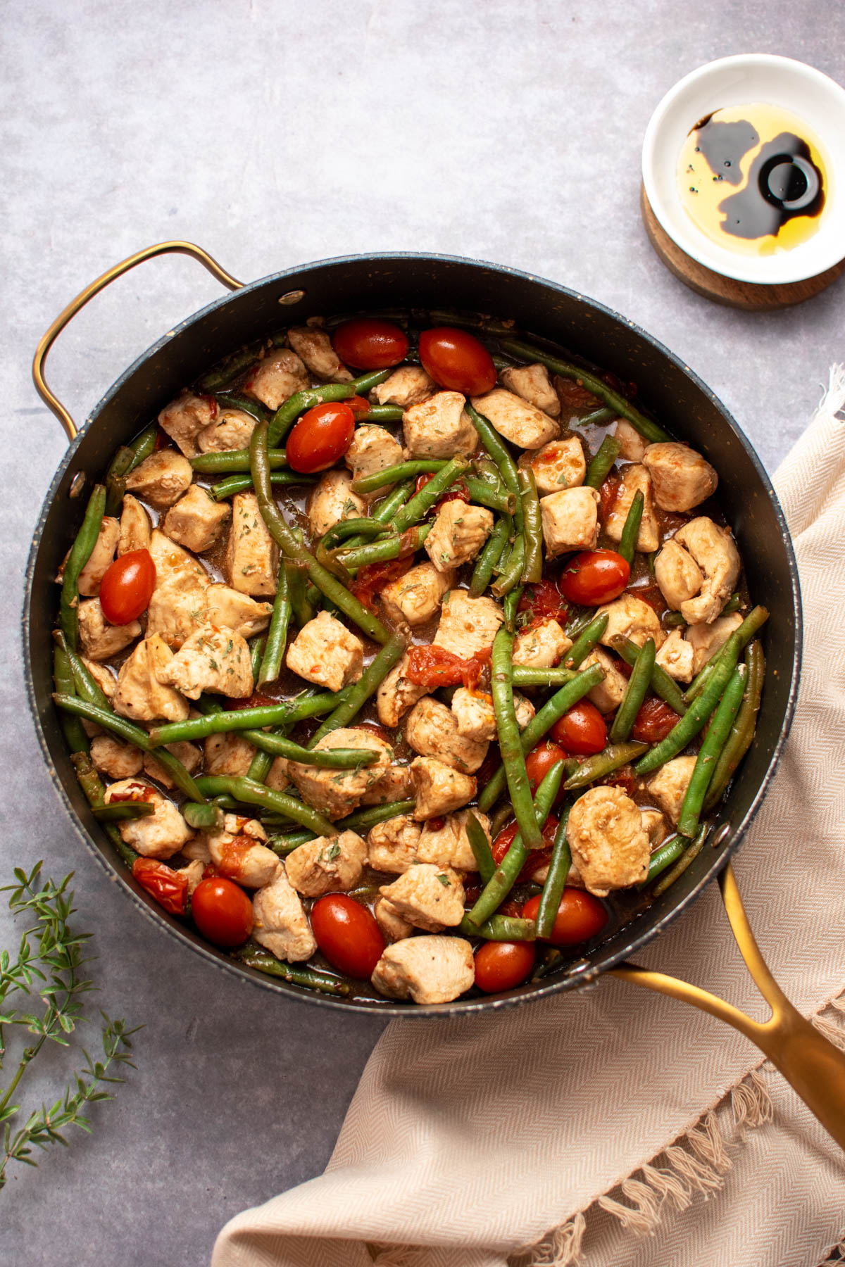 Large black skillet with diced chicken, tomatoes, and green beans on dark table top with tan towel nearby.