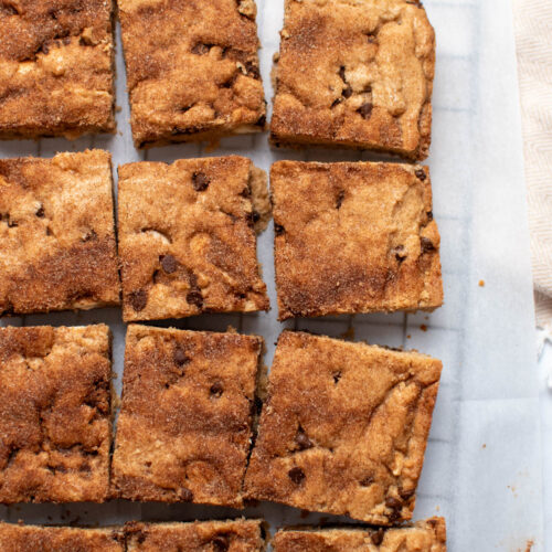 Group of several chocolate chip blondies touching closely on parchment paper.