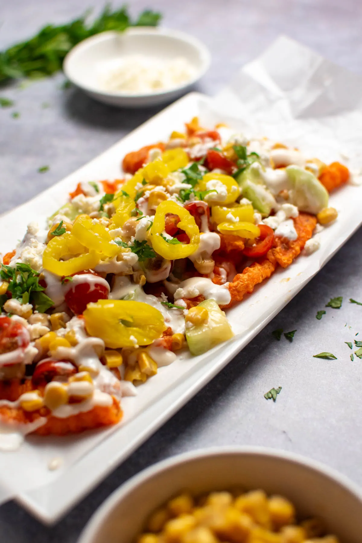 Mediterranean Street Fries with banana peppers, chickpeas, and yogurt dressing on parchment paper lined platter.