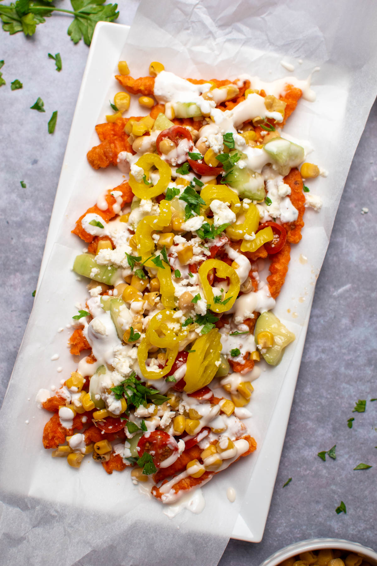 Mediterranean street fries with feta cheese, tomatoes, cucumbers, and banana peppers on white rectangle platter.