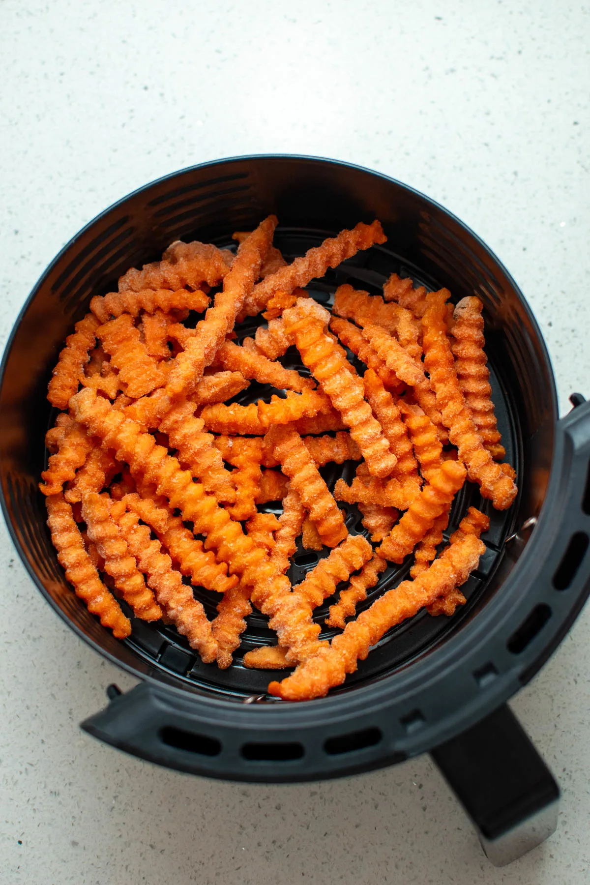 Frozen sweet potato fries in air fryer basket on quartz countertop.