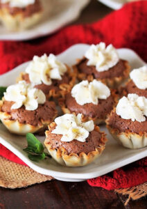 Chocolate chess pie tartlets on white plate.