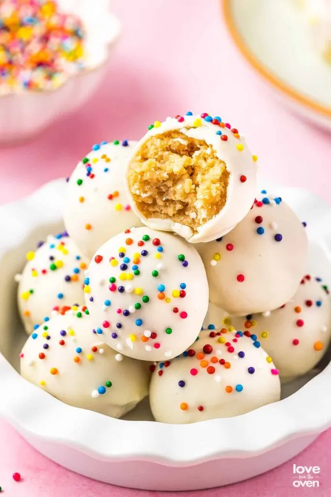 Pile of white cookie truffles with colorful sprinkles in a white bowl.